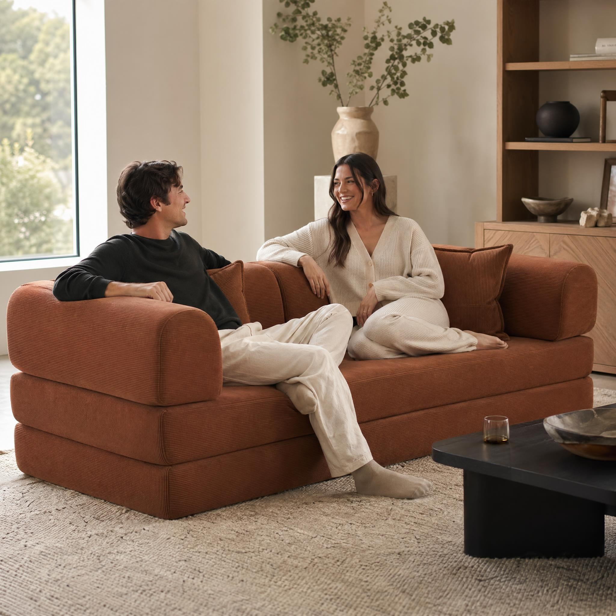 Two people sitting on a the Nüage King Sofa Bed in a living room.